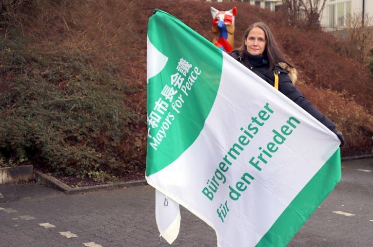Eine Frau hält die Mayors for Peace Flagge in die Kamera